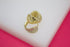 A pair of gold huggie hoop earrings featuring intricate filigree work and sparkling pavé stones rests on a white and pink surface.
