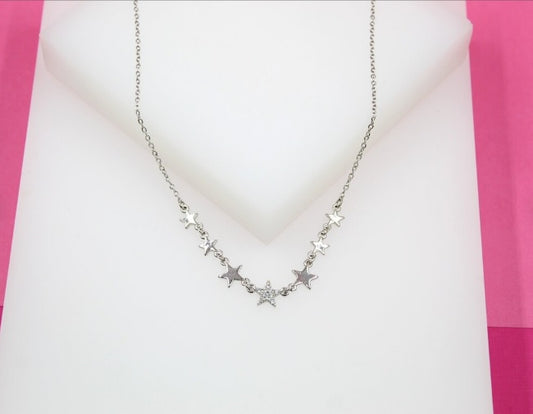 A delicate silver star pendant necklace rests on a white display against a pink background.