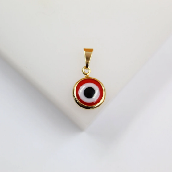 A gold-plated evil eye pendant featuring vibrant red, white, and black enamel rests on a clean white surface.