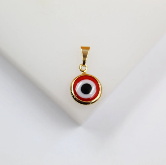 A gold-plated evil eye pendant featuring vibrant red, white, and black enamel rests on a clean white surface.