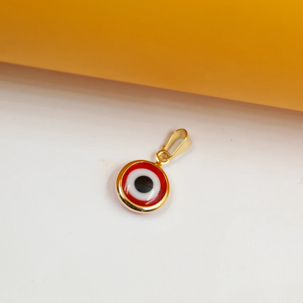 A gold-plated evil eye pendant features concentric circles of red, white, and black enamel against a clean white surface.