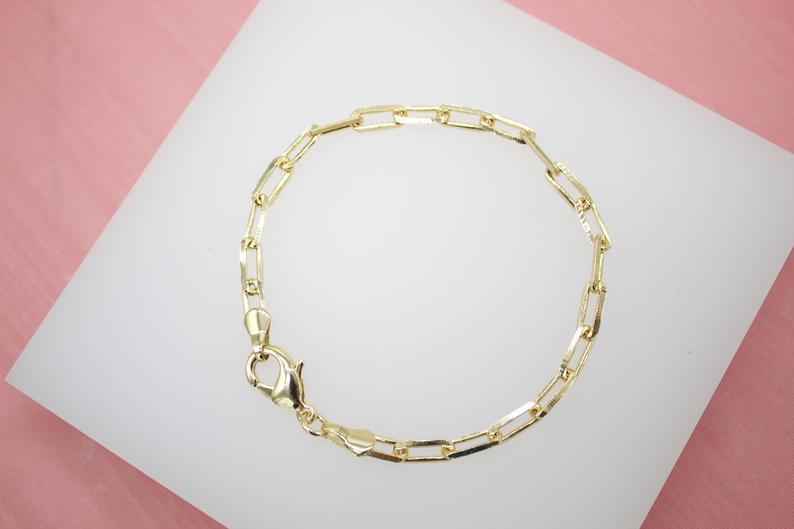 A delicate gold paperclip chain bracelet rests on a white display surface.
