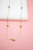 A delicate gold chain necklace features evenly spaced polished bead stations displayed against a pink background.
