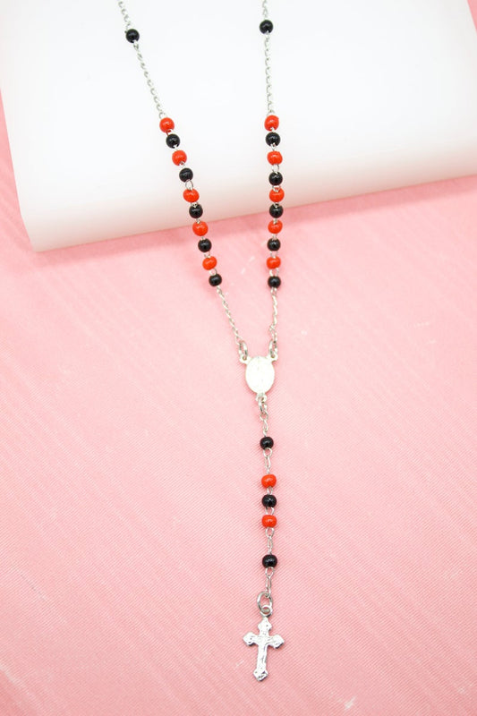 A silver rosary necklace featuring alternating bright red and glossy black beads rests against a pink fabric background.