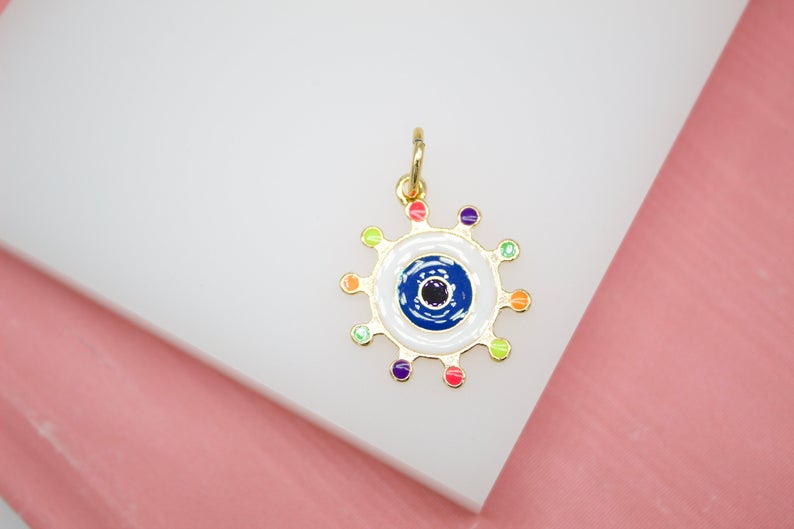 A gold evil eye charm featuring colorful enamel details rests on a white display surface.
