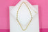 A delicate gold heart-shaped link necklace rests on a white display block against a vibrant pink background.