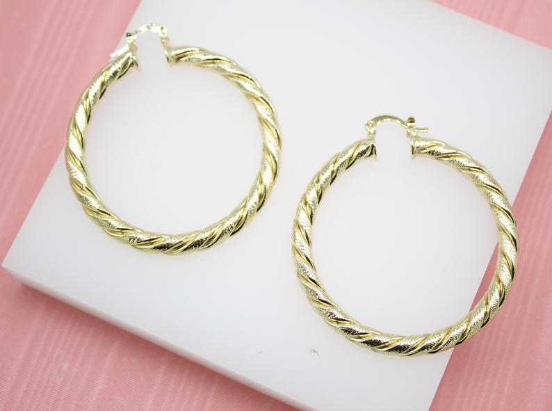A pair of textured gold hoop earrings rests on a white display block.