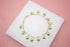 A delicate gold charm bracelet featuring dangling heart pendants rests gracefully on a white display tile against a soft pink background.