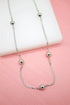 A delicate silver chain necklace features evenly spaced polished bead stations resting against a pink and white background.