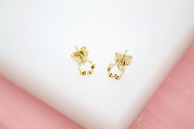 A pair of gold flower stud earrings rests on a white surface.
