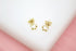 A pair of gold flower stud earrings rests on a white surface.