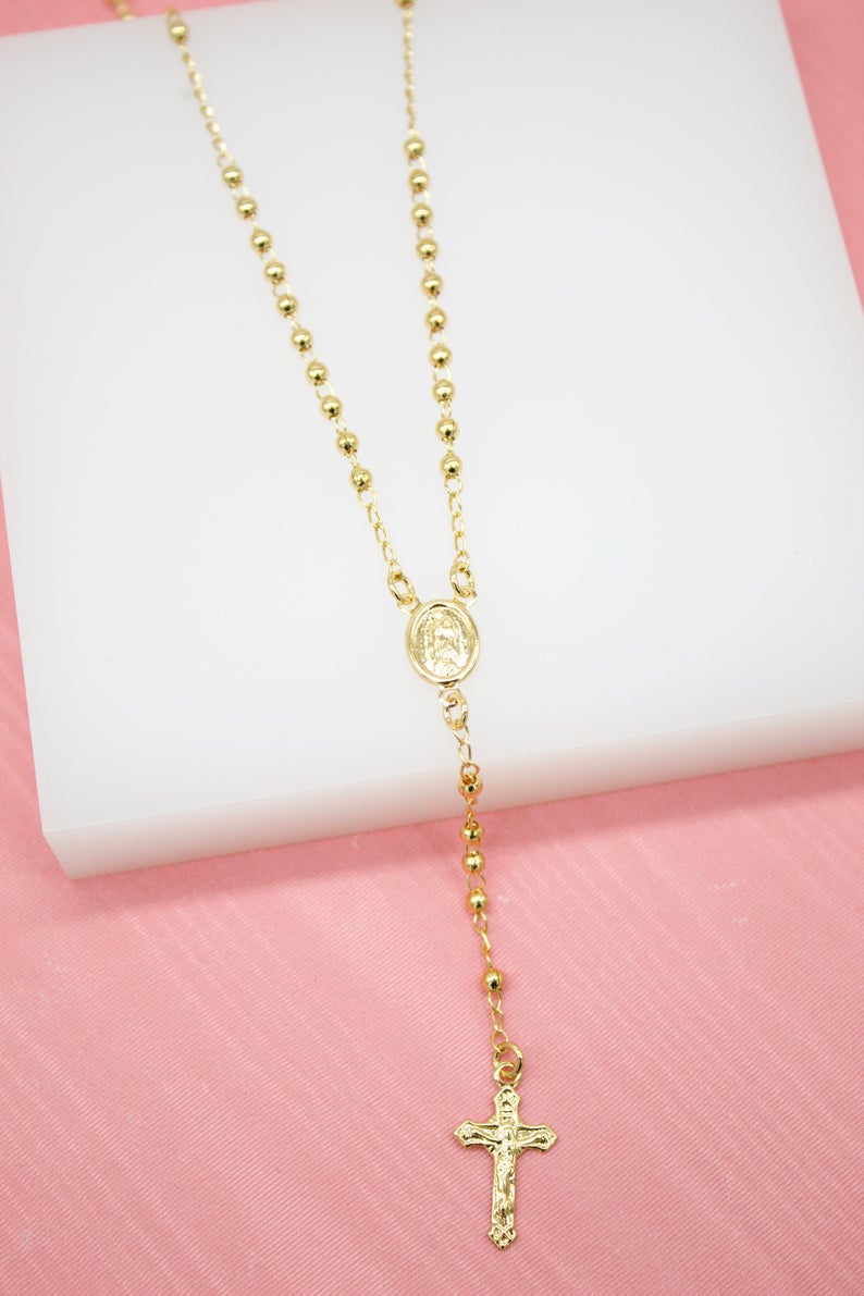 A gold rosary necklace with beaded chains and a crucifix pendant rests on a white display block.