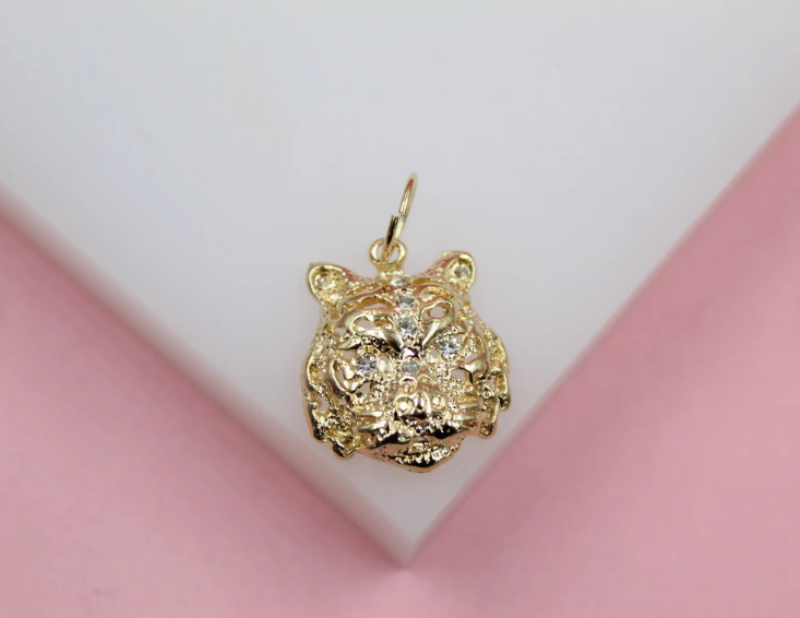 A sparkling gold tiger head pendant rests against a white and pink background.
