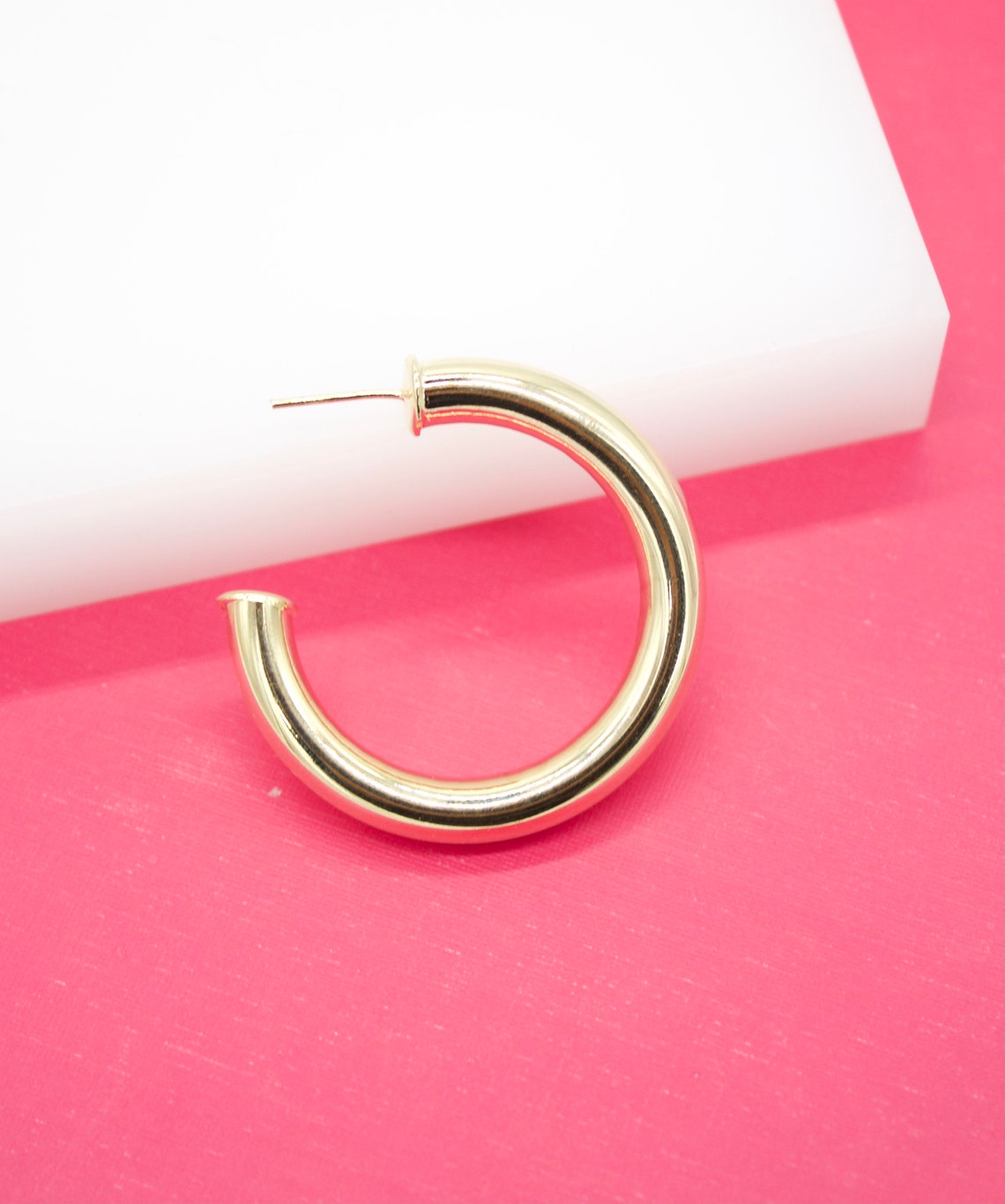 A shiny gold hoop earring rests against a bright pink and white background.