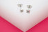 A pair of delicate silver square stud earrings rests on a white and pink display surface.