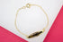 A delicate gold ID bracelet rests on a white and pink surface, showcasing its polished metal plate and fine chain link.