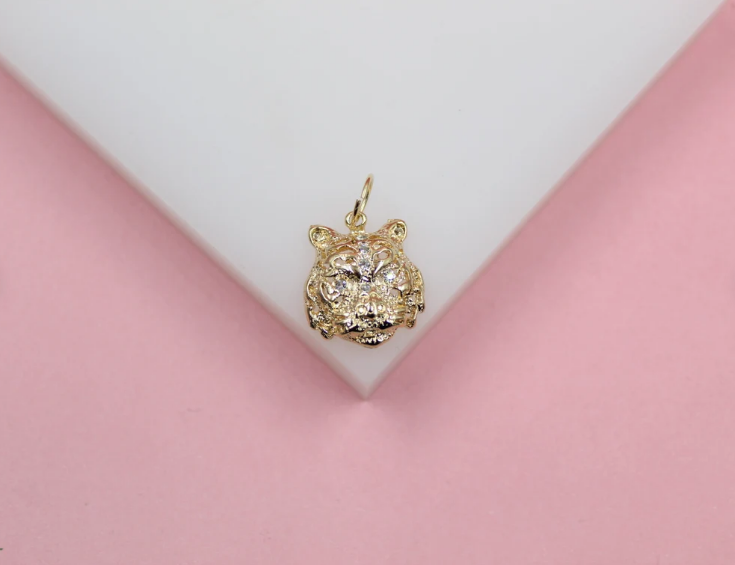 A gold tiger pendant embellished with sparkling pave crystals rests on a white and pink display surface.