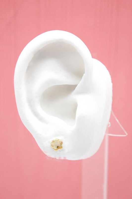 A white display ear model showcases a small gold flower stud earring against a pink background.