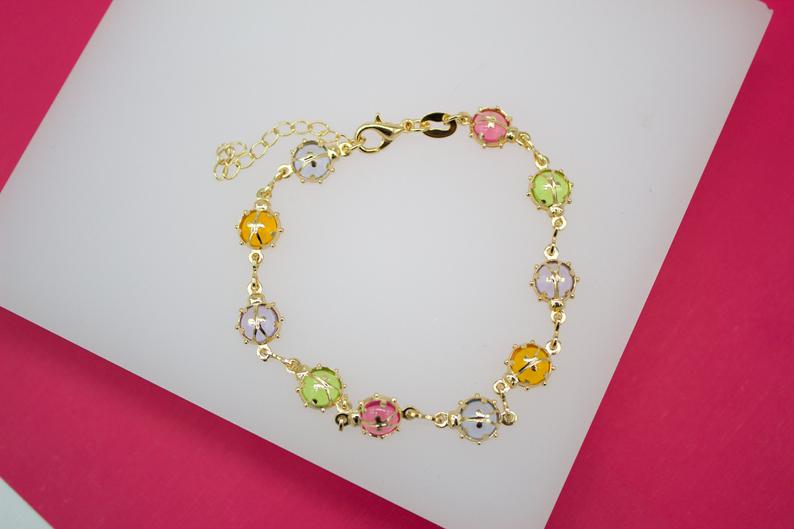 A gold-plated charm bracelet featuring colorful enameled sphere beads rests on a white display surface.