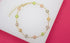 A delicate gold chain bracelet features colorful crystal four-leaf clover charms arranged against a white and pink background.