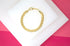A polished gold curb chain bracelet rests elegantly on a white display block against a vibrant pink background.