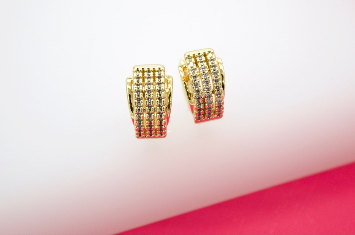 A pair of elegant gold hoop earrings showcases rows of sparkling pave-set stones against a white and pink background.