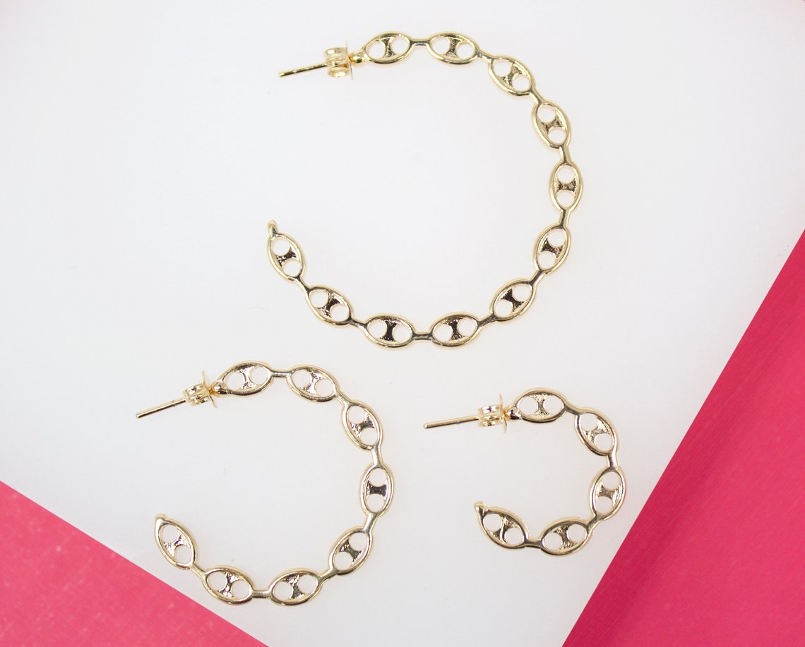 Three gold chain-link hoop earrings of varying sizes rest on a white and pink background.
