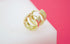 A pair of sparkling gold hoop earrings resting on a white display block against a pink background.