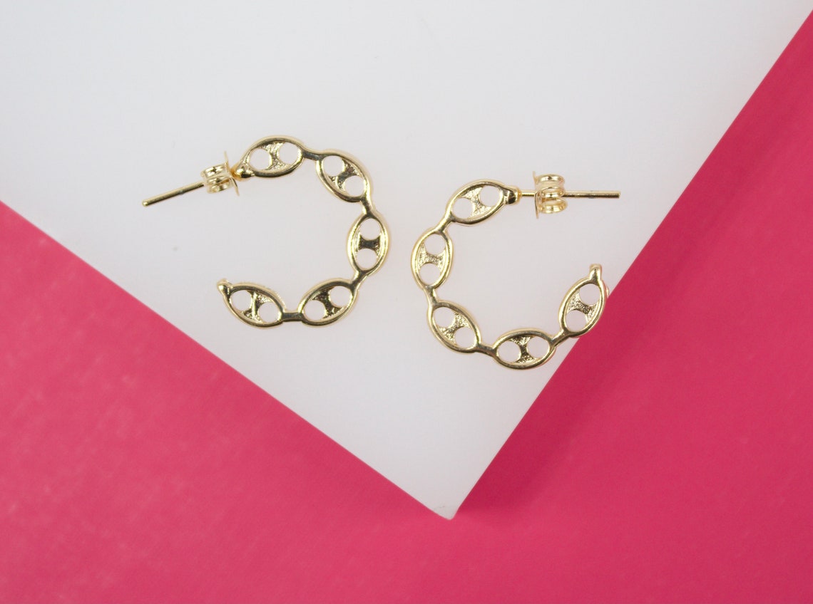 A pair of gold link hoop earrings rests on a geometric white and pink display.