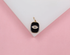 A gold evil eye charm featuring sparkling cubic zirconia stones and black enamel rests on a white display surface against a pink background.