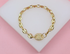 A gold-plated chain bracelet featuring textured oval links rests on a white display surface against a pink background.