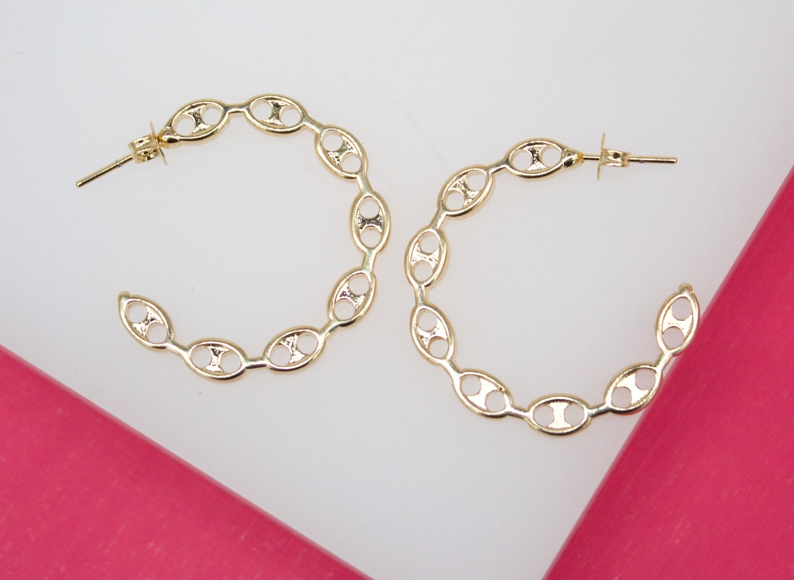 A pair of gold link hoop earrings rests against a bright white background.