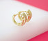 A pair of gold huggie hoop earrings with textured, studded details rests on a white and pink surface.