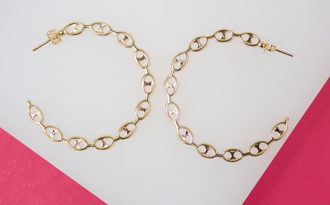 A pair of gold link hoop earrings rests against a white and pink background.