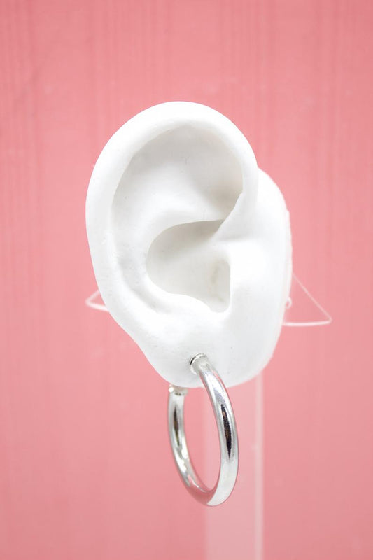 A white mannequin ear displays a polished silver hoop earring against a pink background.