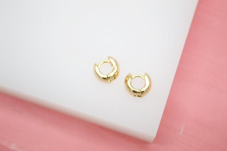 A pair of small gold hoop earrings rests on a white display surface.