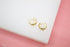 A pair of small gold hoop earrings rests on a white display surface.