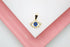 A gold evil eye pendant set with cubic zirconia stones and a bright blue enamel center rests on a white and pink surface.