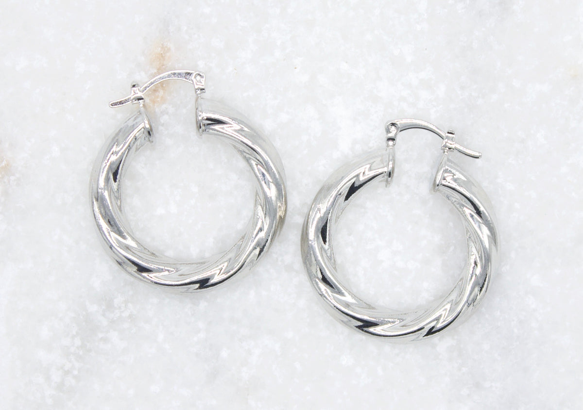A pair of polished silver twist hoop earrings rests against a white textured background.