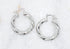 A pair of polished silver twist hoop earrings rests against a white textured background.