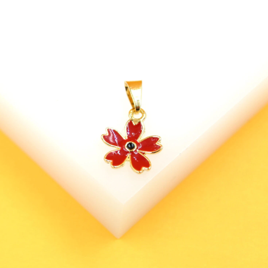 A gold-rimmed red flower pendant with a dark center rests on a white display surface against a yellow background.
