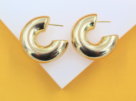 A pair of chunky gold hoop earrings rests on a white and yellow geometric display surface.