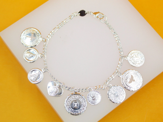 A silver charm bracelet featuring multiple religious medallions, including a cross and a heart, rests on a white display pad against a yellow background.