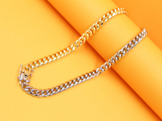 A sleek two-tone cuban link chain displays a seamless blend of gold and silver finishes against a vibrant yellow background.