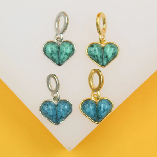 Four heart-shaped turquoise stone charms in gold and silver settings rest on a display stand.