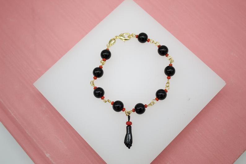 A gold charm bracelet features black beads and a figa fist pendant displayed on a white surface.