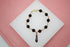 A gold charm bracelet features black beads and a figa fist pendant displayed on a white surface.