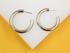 A pair of thick silver hoop earrings rests on a white display against a vibrant yellow background.