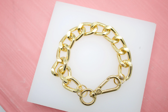 A chunky gold chain bracelet rests on a white display pad against a pink background.