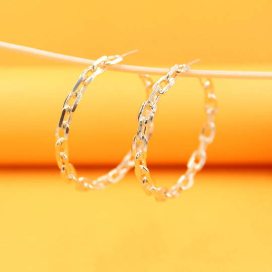 Two shiny gold chain link hoop earrings hang gracefully from a thin stick against a vibrant yellow background.